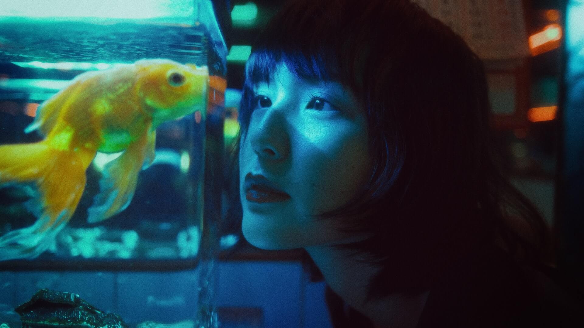 A talented lady is looking at a fish in an aquarium